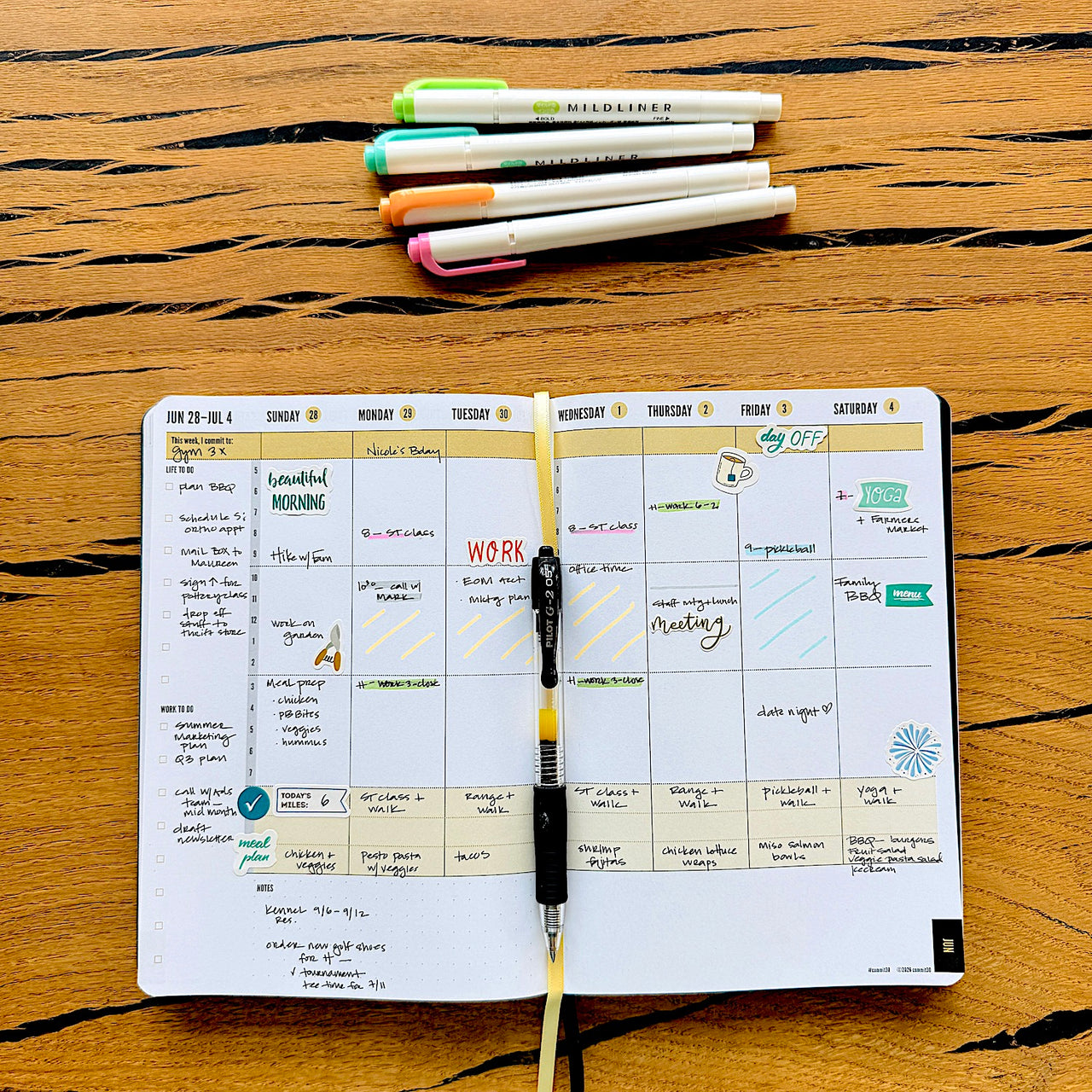 Open 2026 planner with daily schedule on a wooden surface, surrounded by pens.